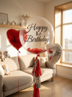 Прозрачный шар Bubble с черной надписью Happy 1st Birthday, красными перьями внутри и фольгированными сердцами в интерьере.