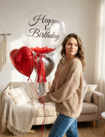 Прозрачный шар Bubble с черной надписью Happy 1st Birthday, красными перьями внутри и фольгированными сердцами в интерьере.