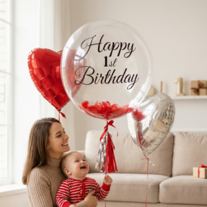 Прозрачный шар Bubble с черной надписью Happy 1st Birthday, красными перьями внутри и фольгированными сердцами в интерьере.